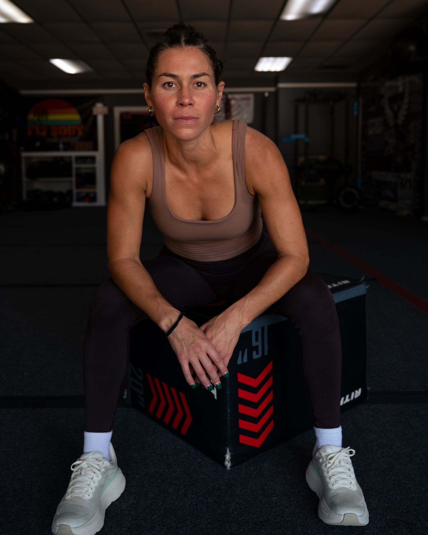 Athletic person in black workout attire and white sneakers crouches in a gym setting during exercise routine.