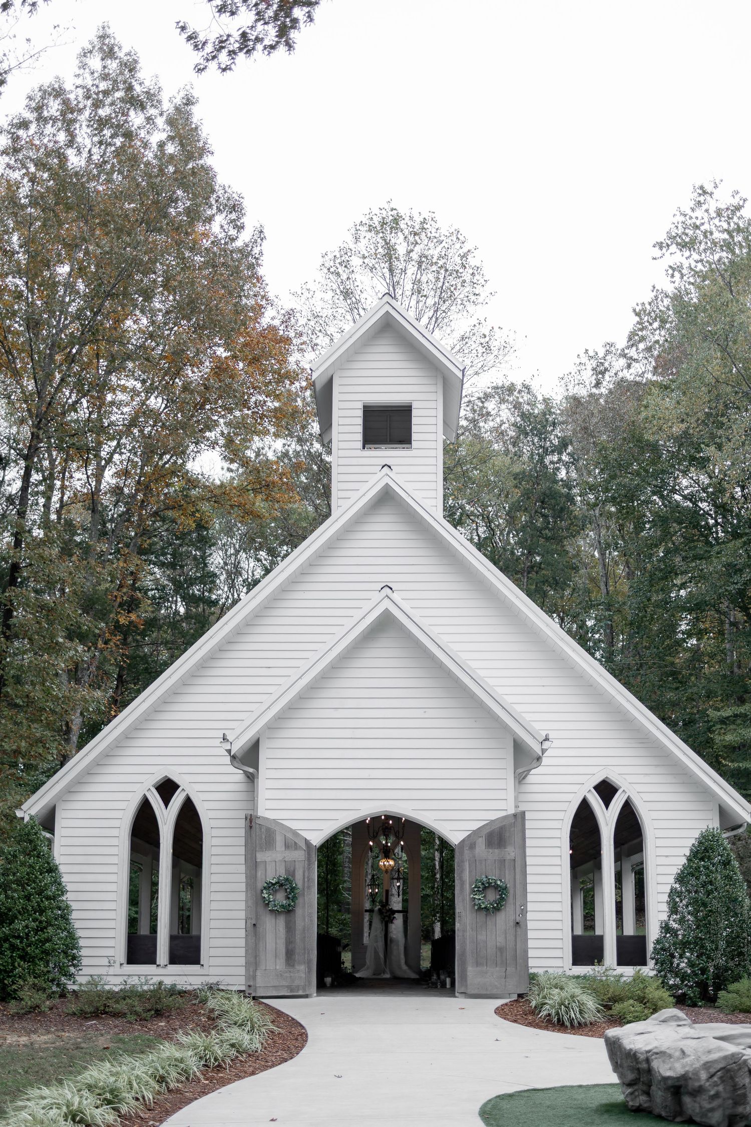 A white wedding dress hangs on display along a garden path lined with trees and string lights in an outdoor venue.