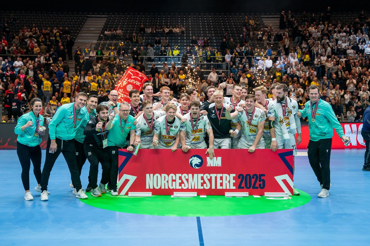 Handball players celebrate on a bright blue court during an intense match.