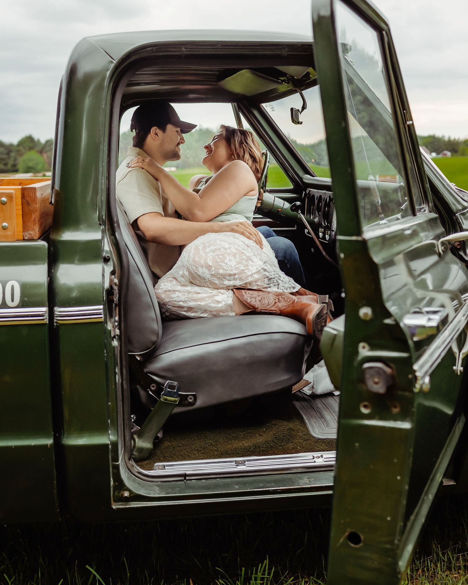 A couple shares a tender moment in the front seat of a vintage green pickup truck in a rural field.