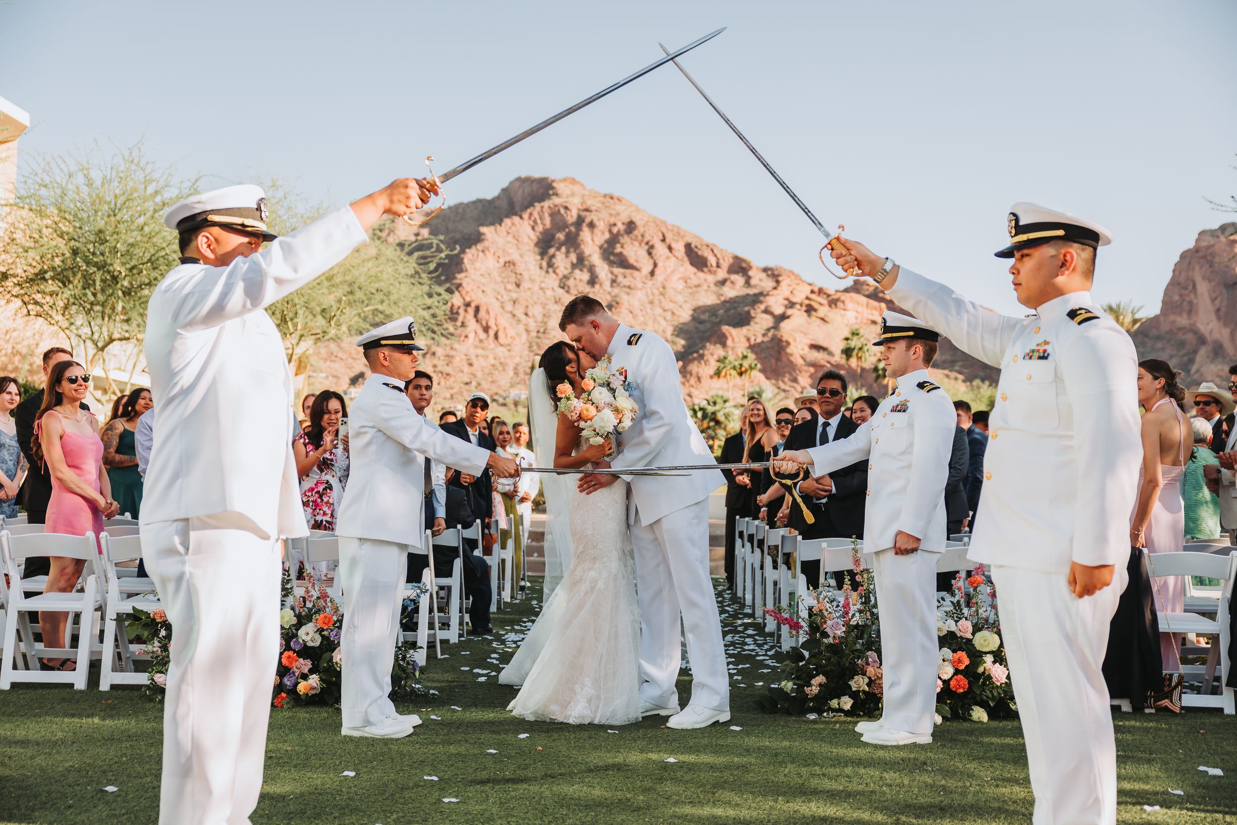 Wedding guests in white attire dancing at an outdoor reception with rock formations in the background at sunset.