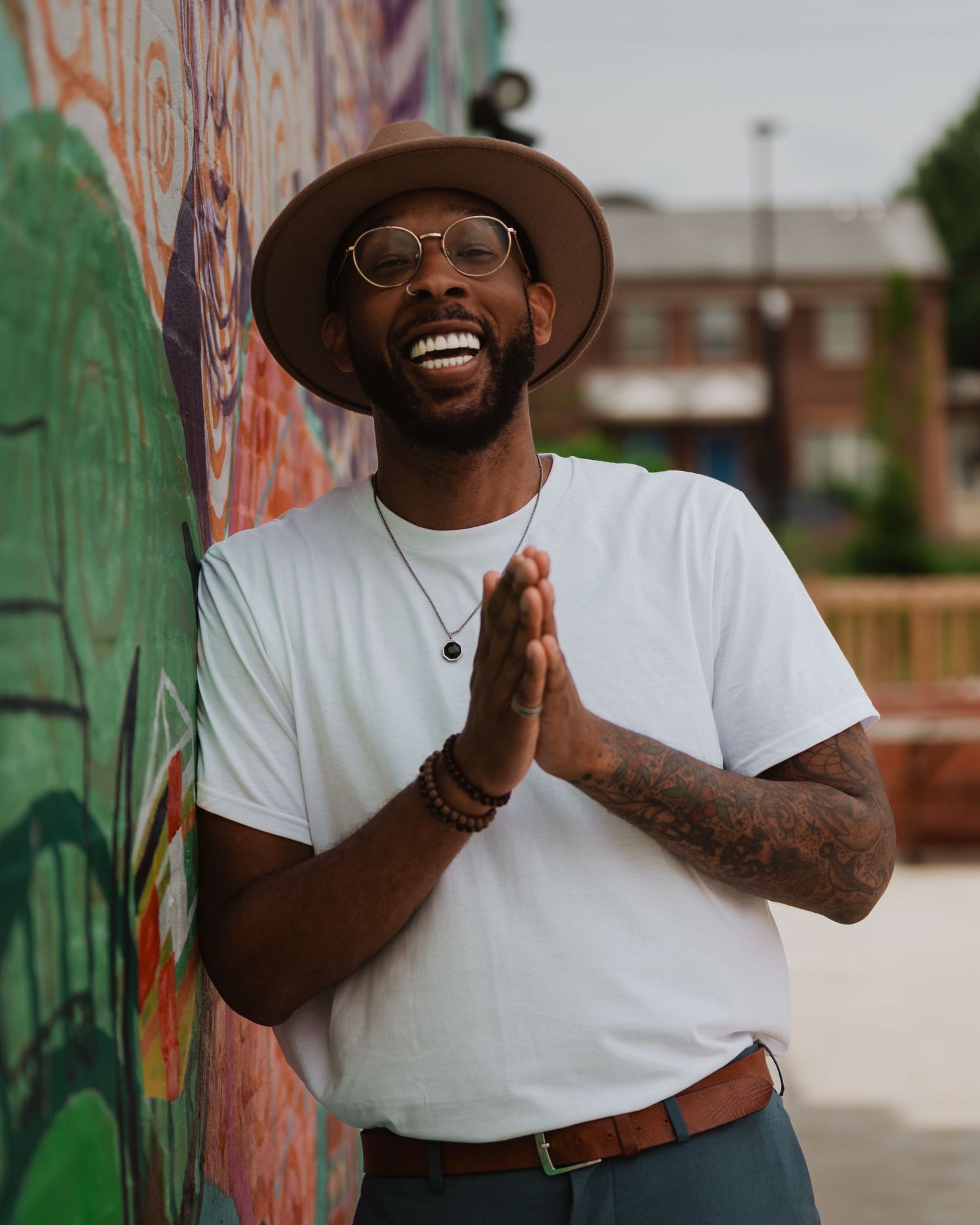 Person in white t-shirt and brown hat showing expressions while posing against colorful graffiti wall outdoors.