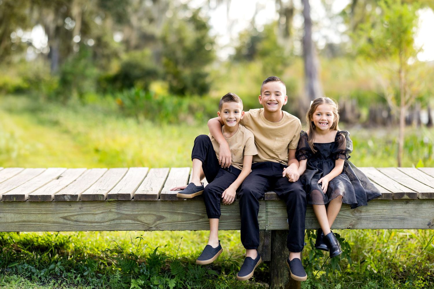 Group of people sitting together on a rustic wooden bench in a sunny outdoor setting.