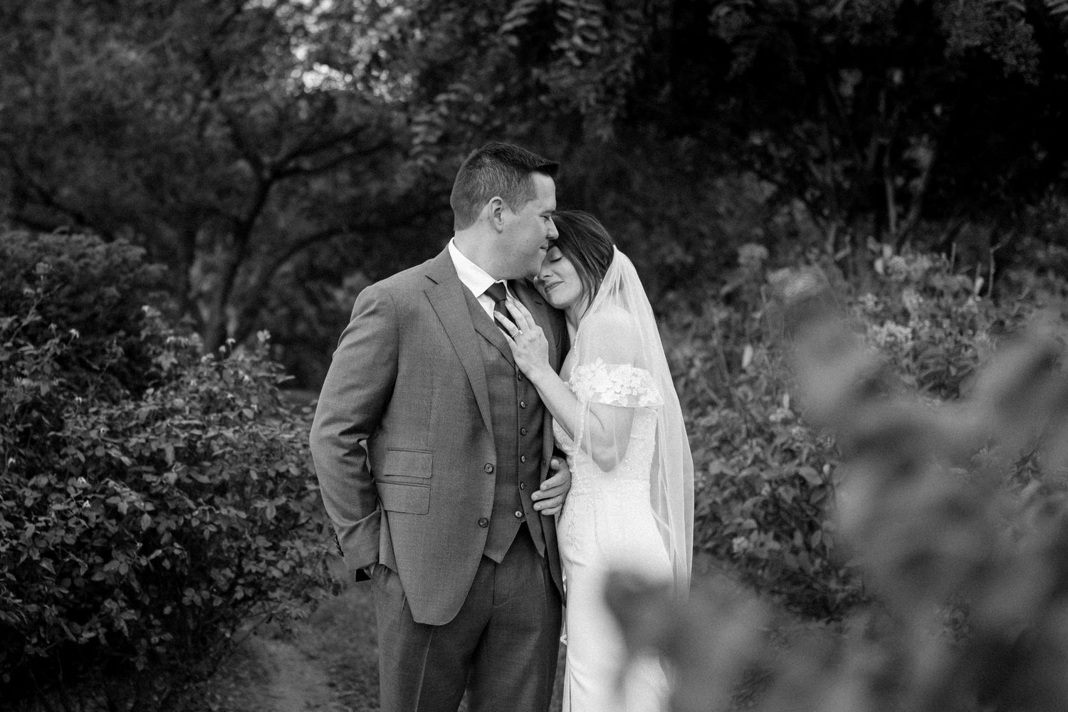 A romantic black and white photo series of a couple embracing in a garden setting during a wedding celebration.