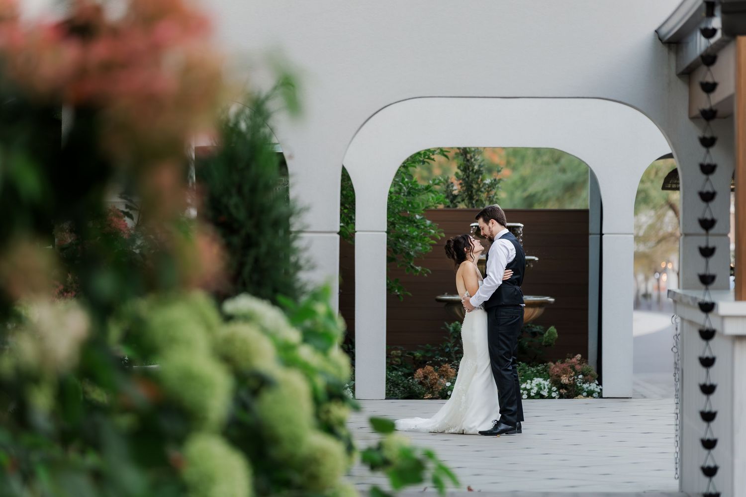 Wedding couple poses under elegant white archway decorated with hanging hearts.