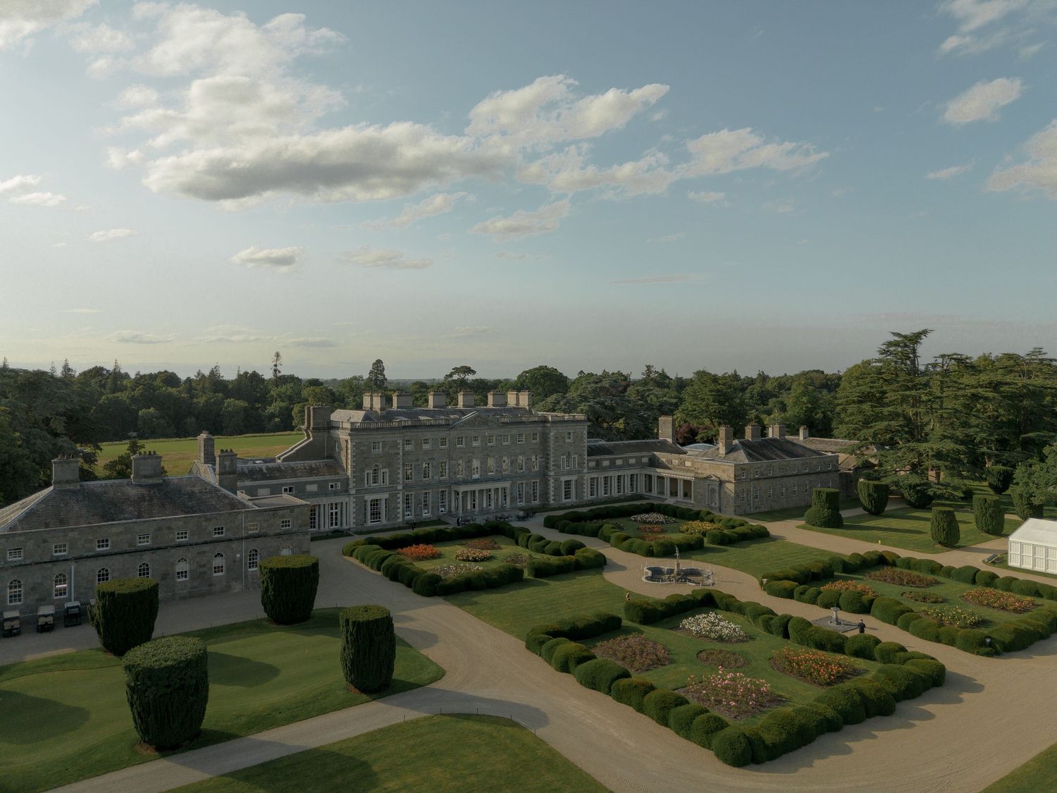 Panoramic view of a formal garden landscape with manicured hedges and curved pathways under a cloudy blue sky.