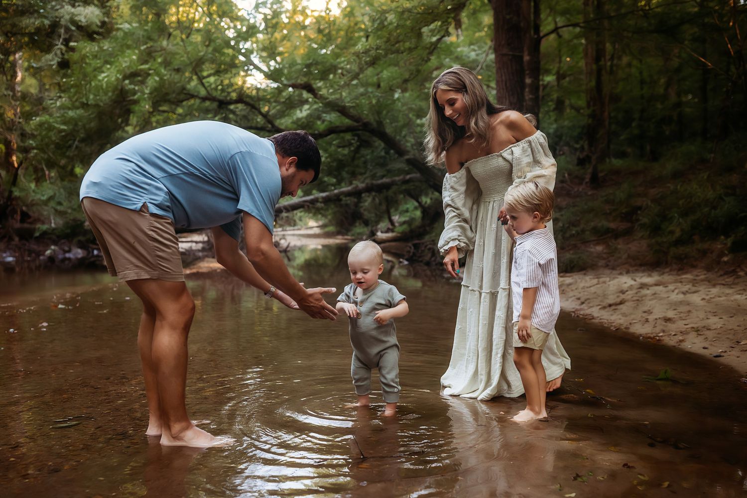Family members playing and splashing together in a shallow creek on a sunny summer day.