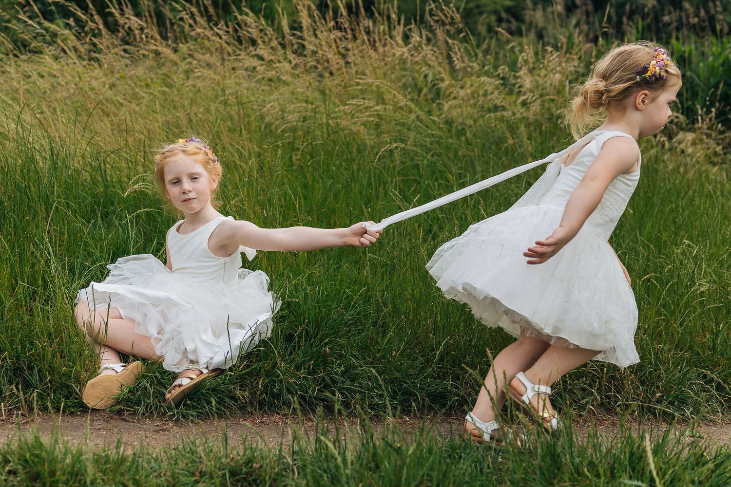 Two children in white dresses playing together in tall summer grass.