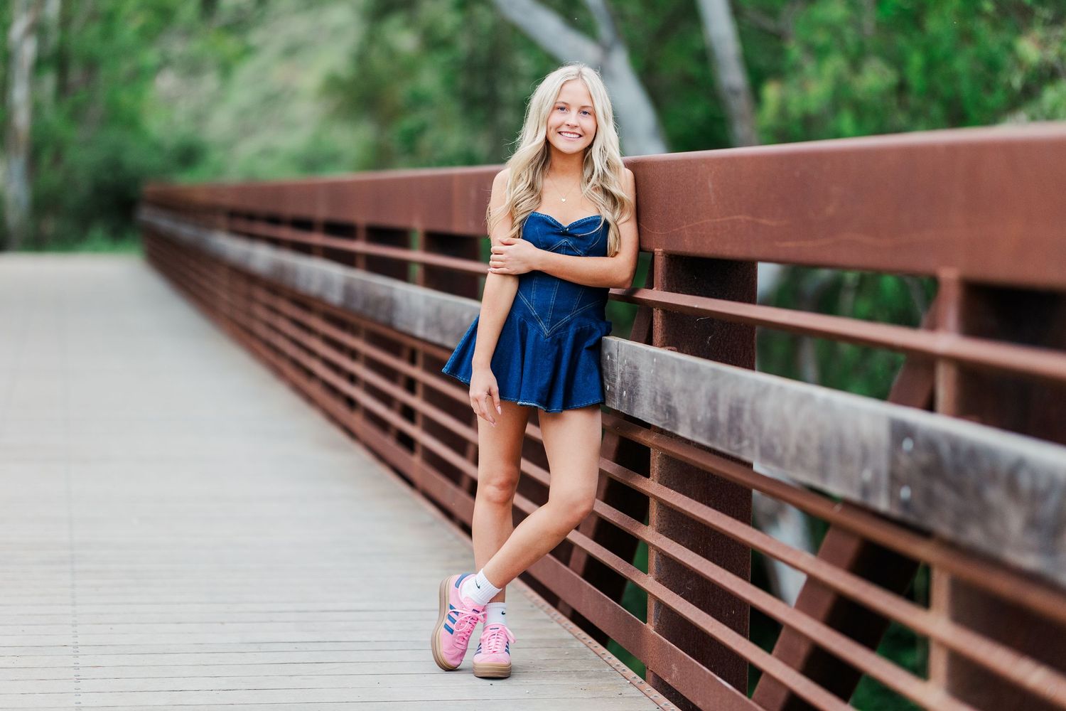 A person in a navy blue dress poses on a wooden bridge walkway in an outdoor setting.
