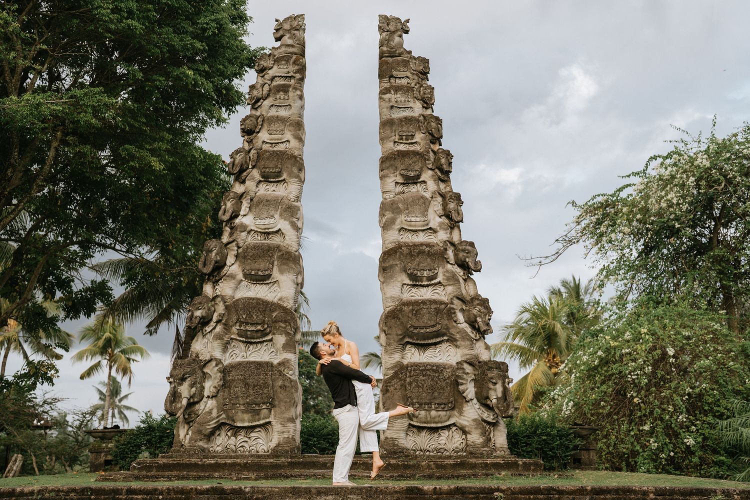 Couple enjoying views from elevated wooden deck with traditional Balinese statues in background.