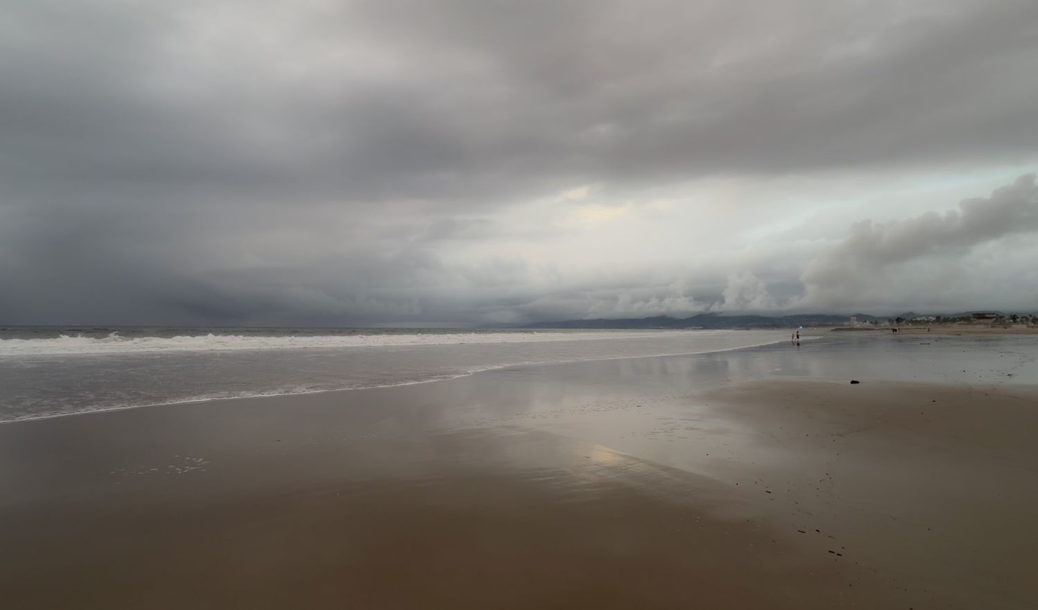 Dramatic cloudy skies over a vast sandy beach with waves rolling in at dusk along the Pacific Northwest coast.