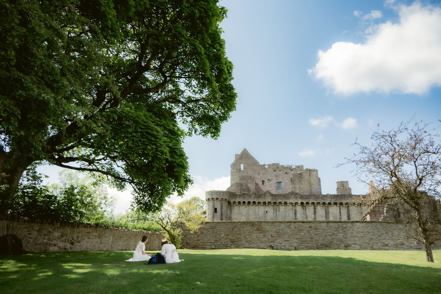 girls in white dresses picnic on the lawn with castle craigmiller in the background, edinburgh