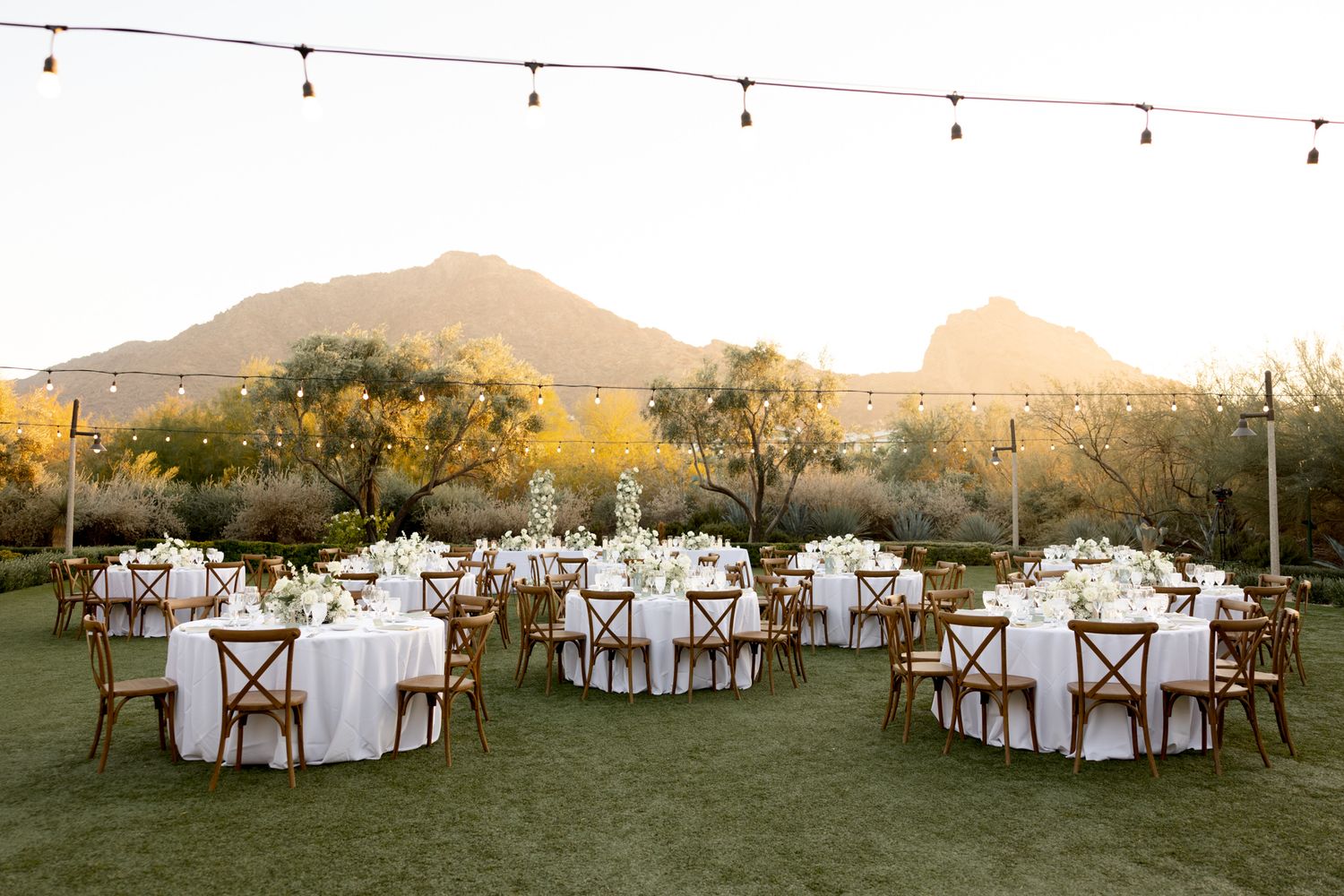 Guests seated at an outdoor desert wedding ceremony with white floral arrangements lining the aisle at sunset.