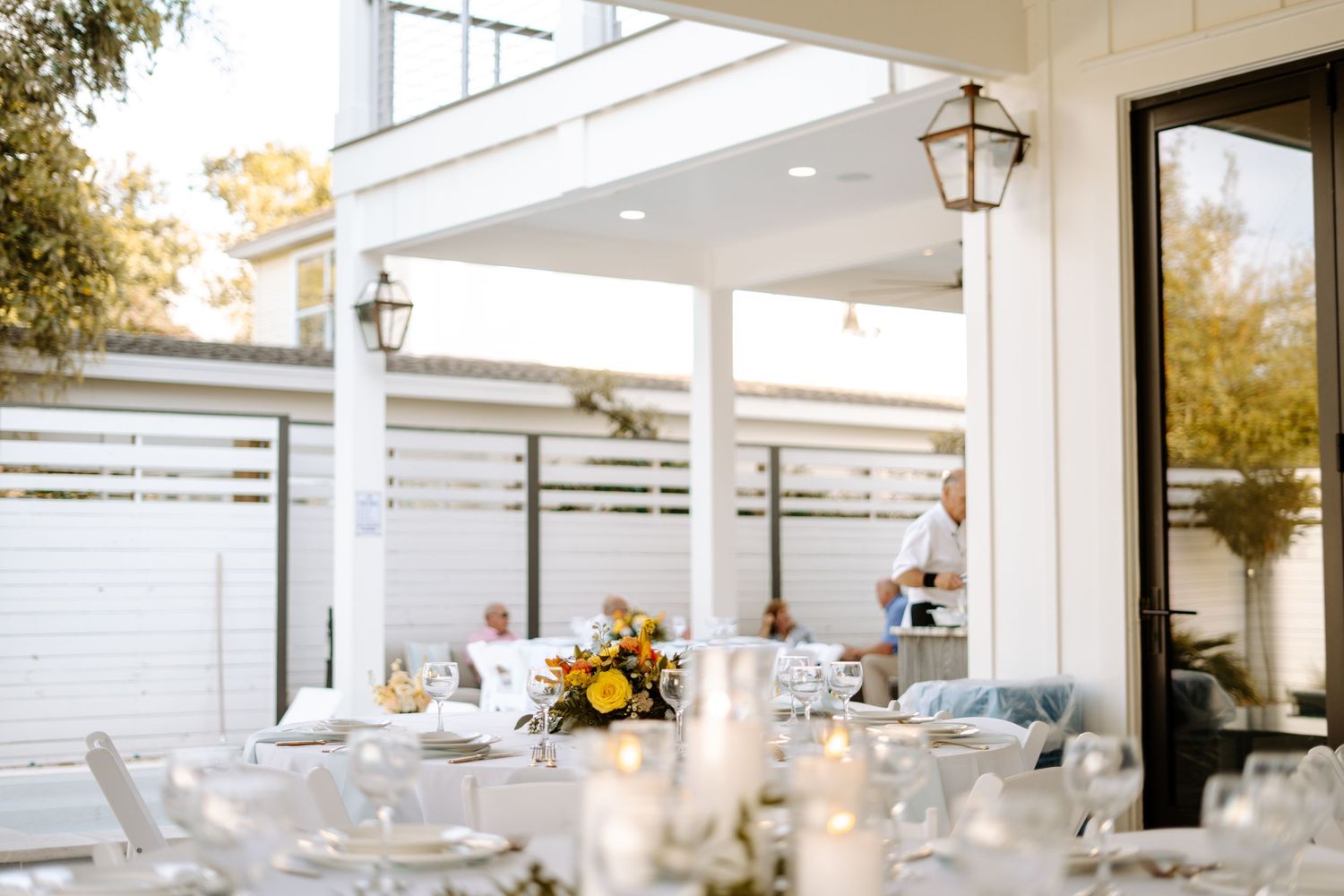 Romantic outdoor wedding reception setup with white furniture and glowing lanterns under an elegant white pergola.