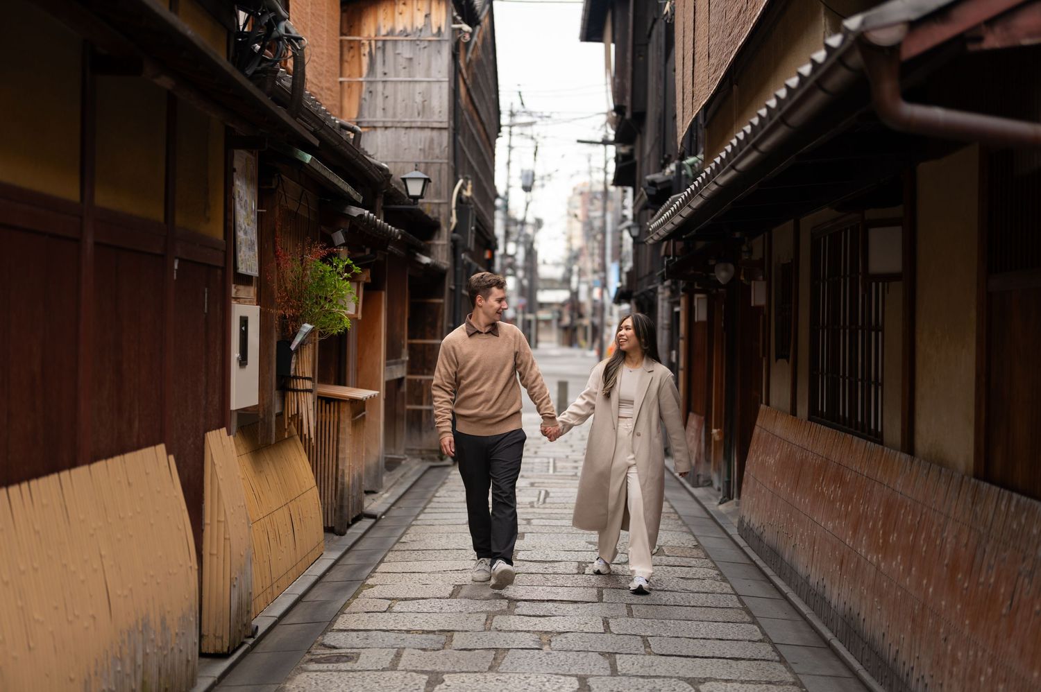 Couple holding hands walking down a traditional cobblestone alley in Kyoto, Japan.