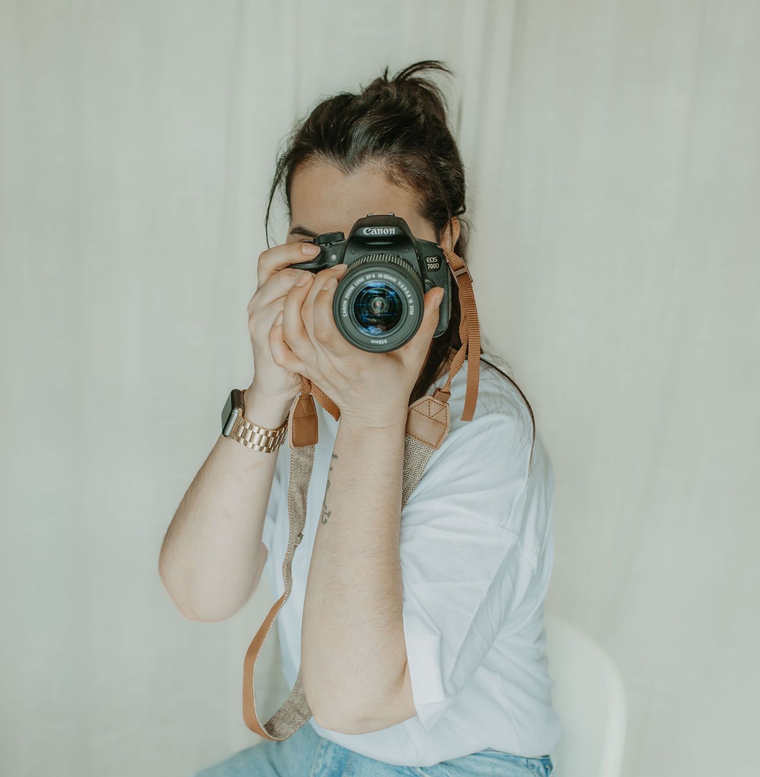 Photographer in white shirt takes photos with professional camera against neutral wall in artistic composition.