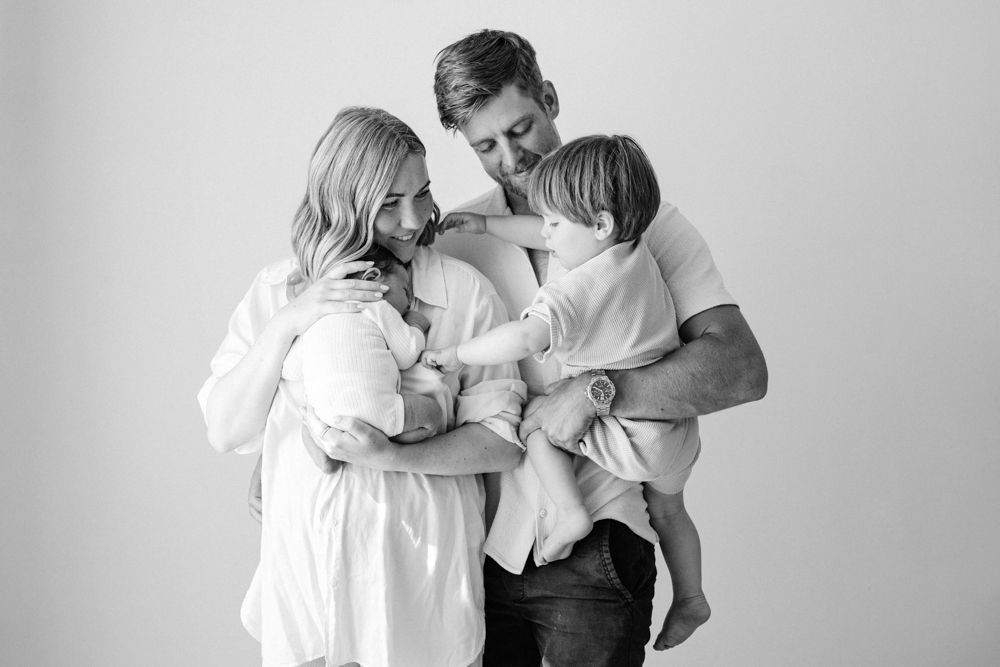 A black and white portrait of a family sharing an intimate moment together against a light background.