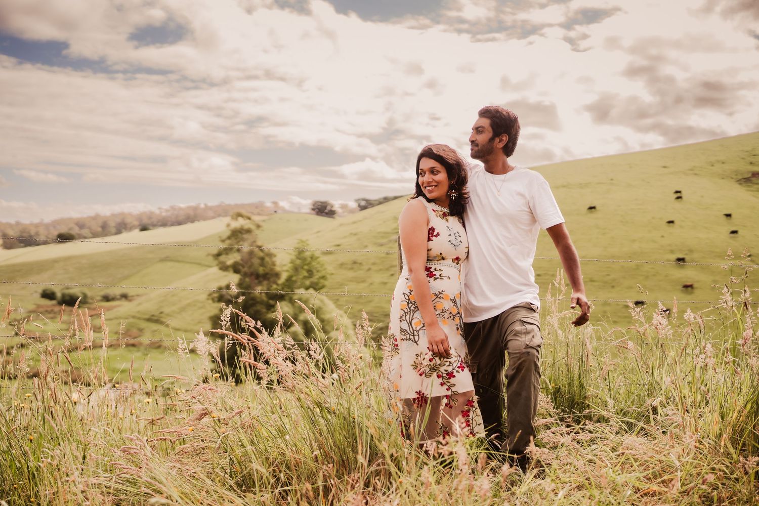 A couple walks together through a scenic hillside meadow on a cloudy afternoon.