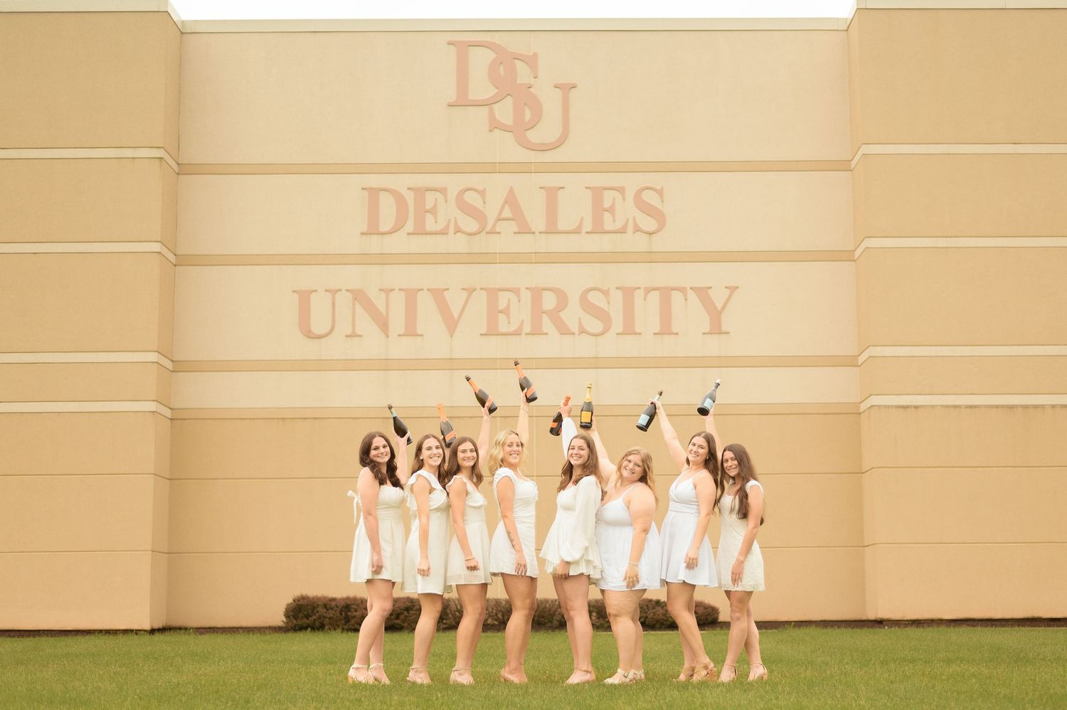 A line of graduates in white dresses pose outside the Gambet Center building.