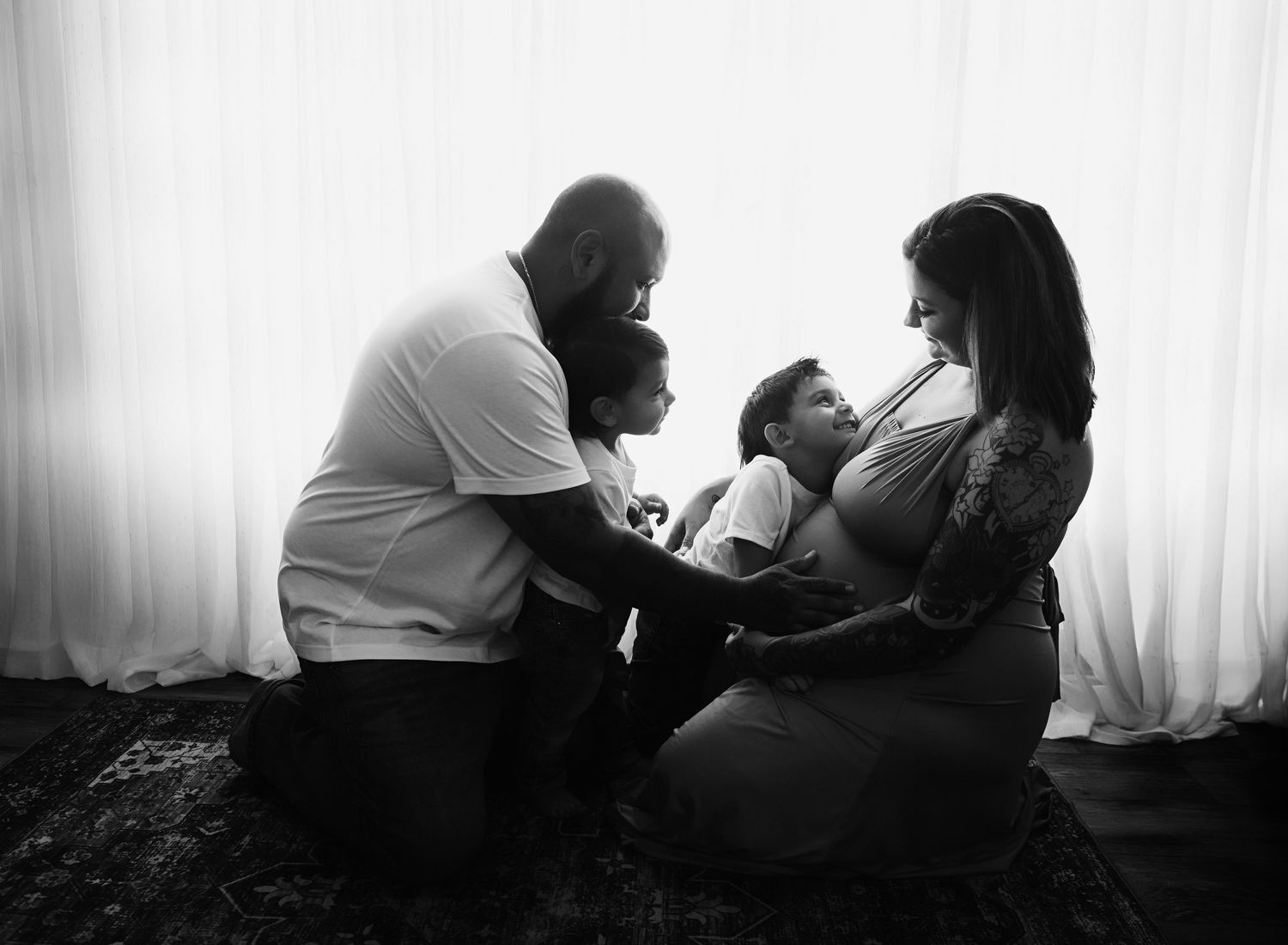 Black and white photograph of a family sharing an intimate moment together by a window at home.