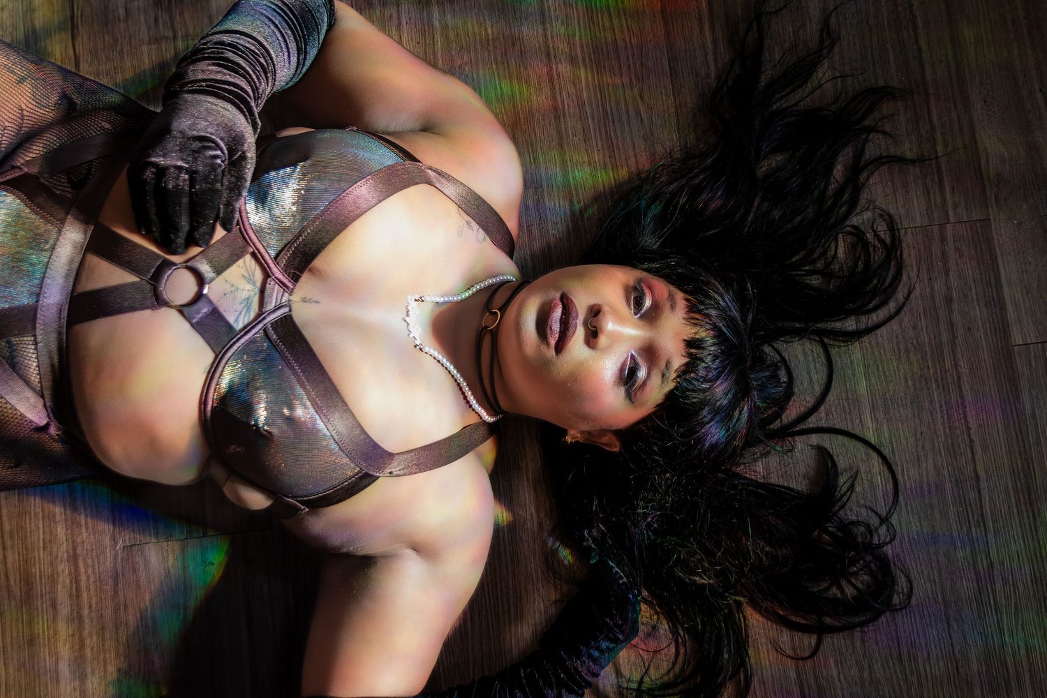 Person with long dark hair wearing an ornate costume laying on a wooden floor.