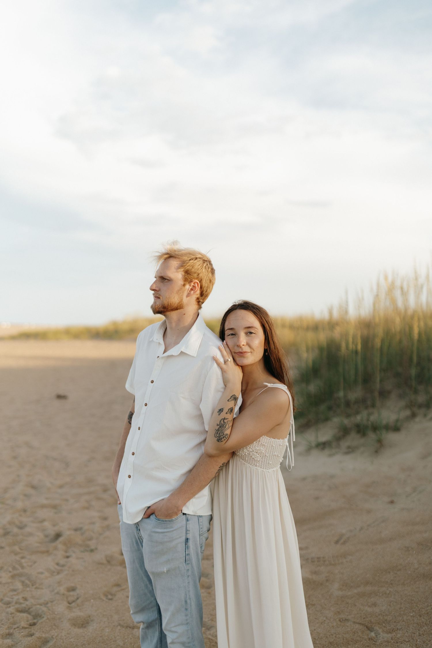 A couple embraces tenderly while standing on a sandy beach during golden hour.