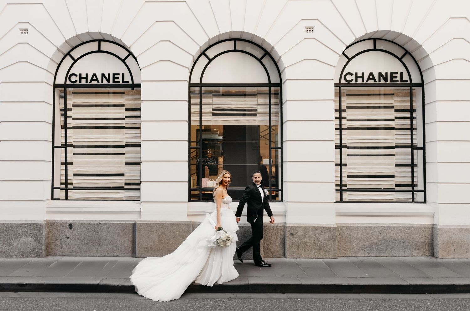 An elegant wedding photoshoot outside a luxury Chanel store with classic arched windows and stone architecture.