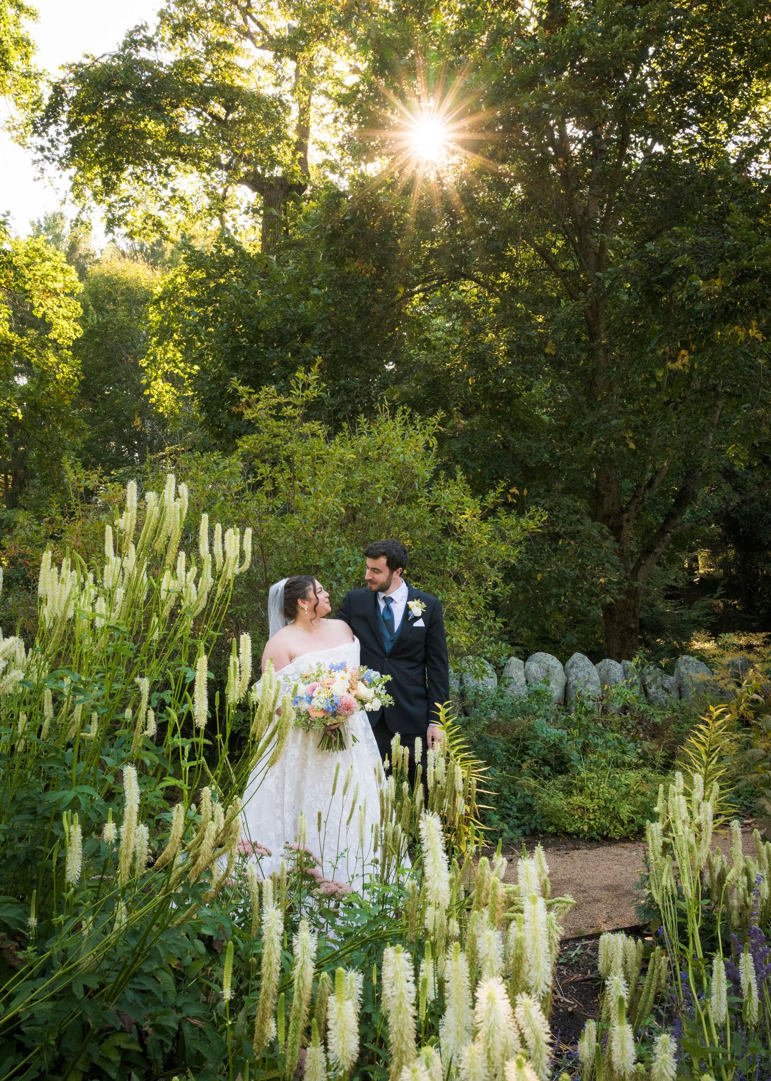 A couple share clear umbrellas on their rainy wedding day in front of a Victorian garden gazebo.