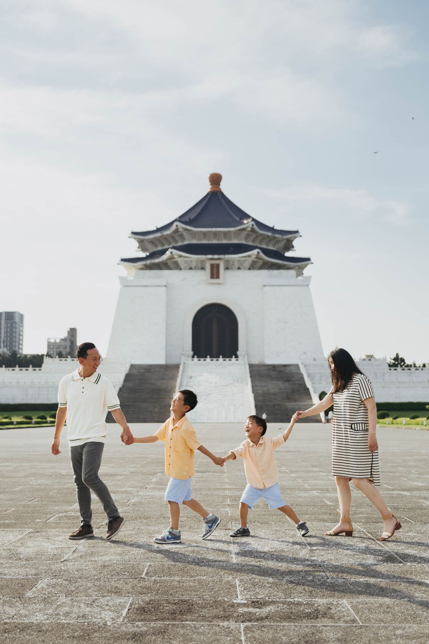 Family of four holds hands walking in front of Chiang Kai-shek Memorial Hall in Taipei, Taiwan.
