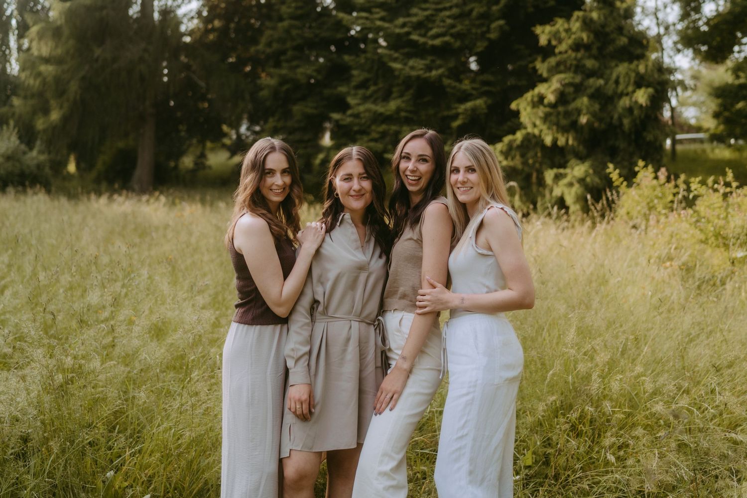 Group of friends in neutral dresses laughing together in a sunlit meadow.