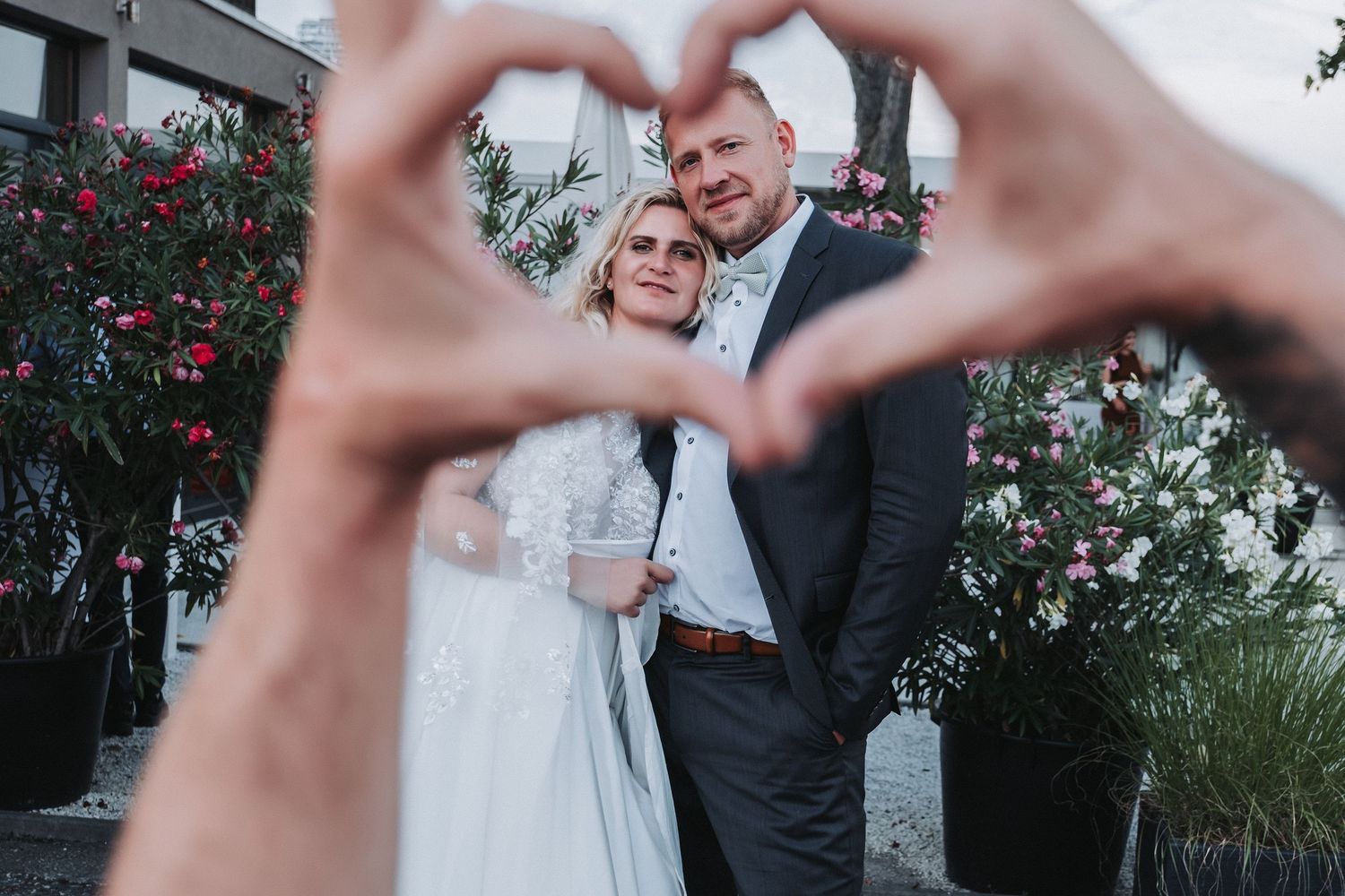 A couple in wedding attire dances together in a garden setting with red roses in the background.