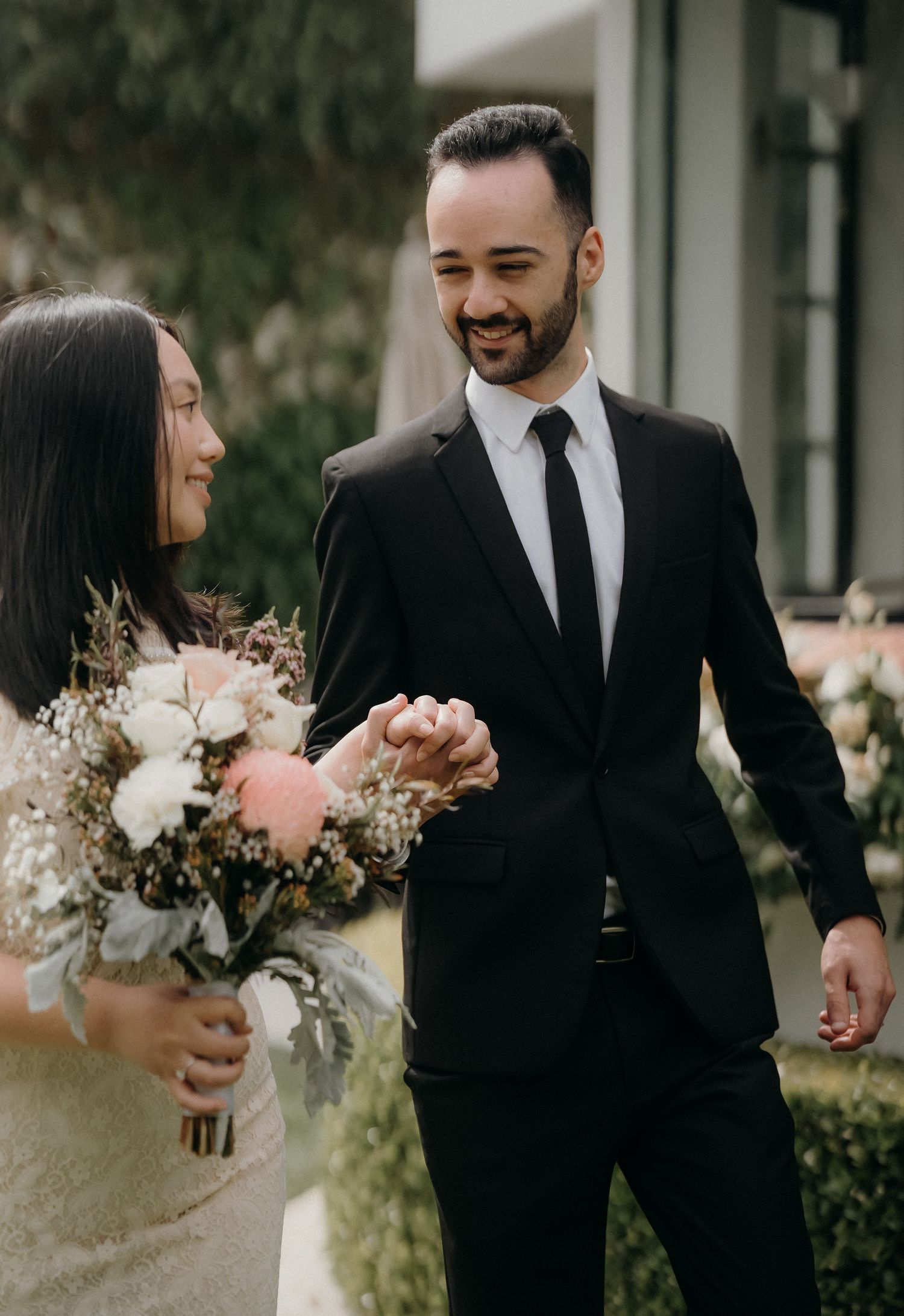 A romantic wedding couple shares joyful moments together in a garden setting with a beautiful floral bouquet.
