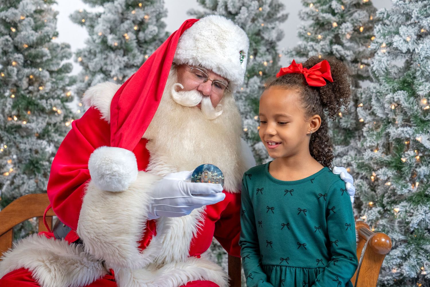 A child in a green sweater sits with Santa Claus in front of a decorated Christmas tree during a holiday photo session.