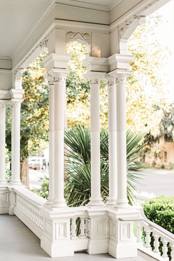 White colonial porch with ornate columns and railings features lush greenery and palm plants in the background at the McHenry Mansion