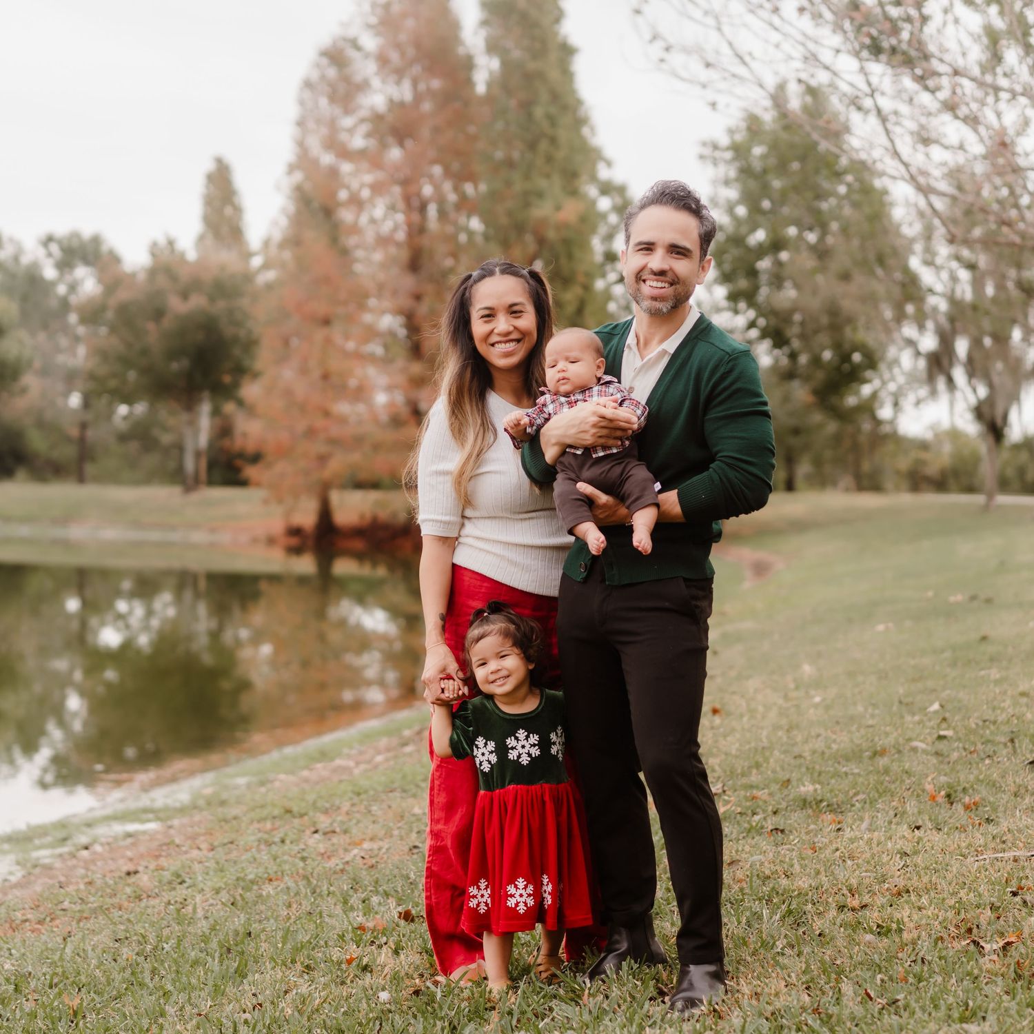 A couple in a grassy field with autumn trees in the background during a fall photo session.
