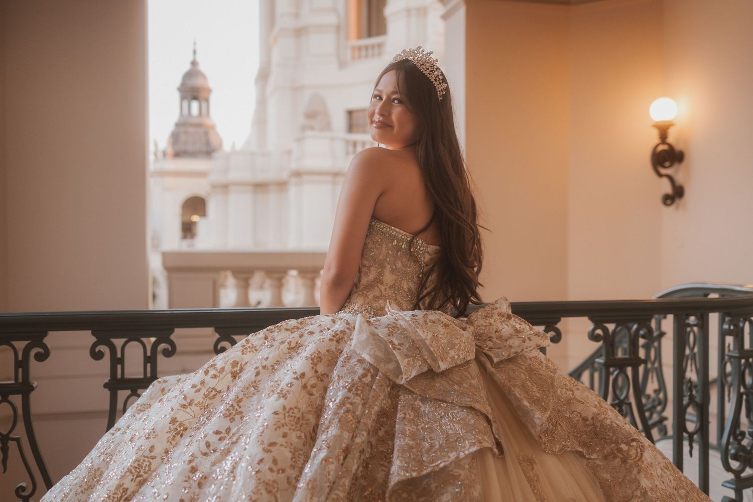 Elegant white lace ballgown with intricate details photographed against ornate balcony with church spire in background.