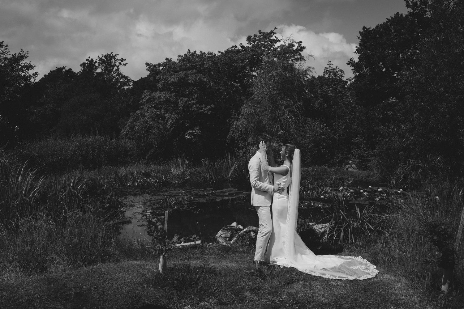Wedding party in coordinated pastel outfits poses together on a grassy lawn under cloudy skies.
