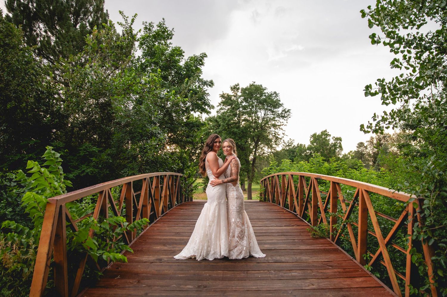 Newlyweds share tender moment on rustic wooden bridge surrounded by lush green trees on wedding day.