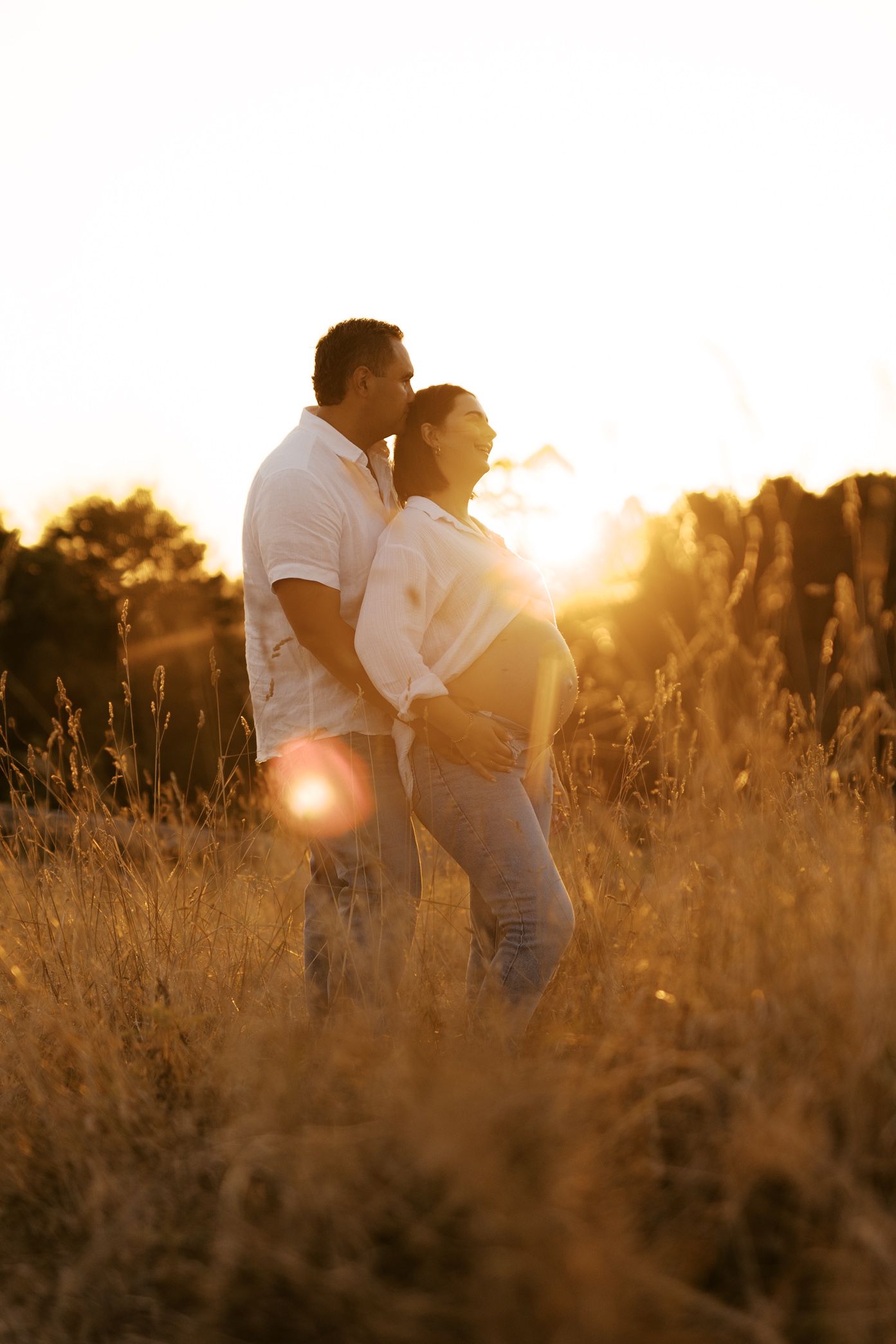 A couple embraces in a golden field during sunset creating a romantic silhouette against the warm glowing sky.