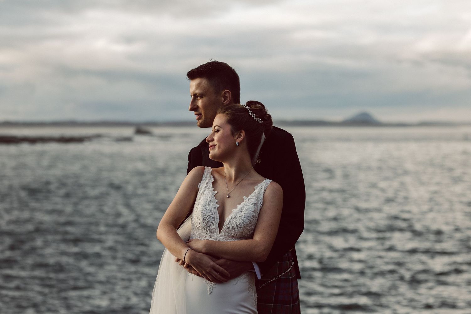 Couple embraces on rocky coastline during overcast evening.