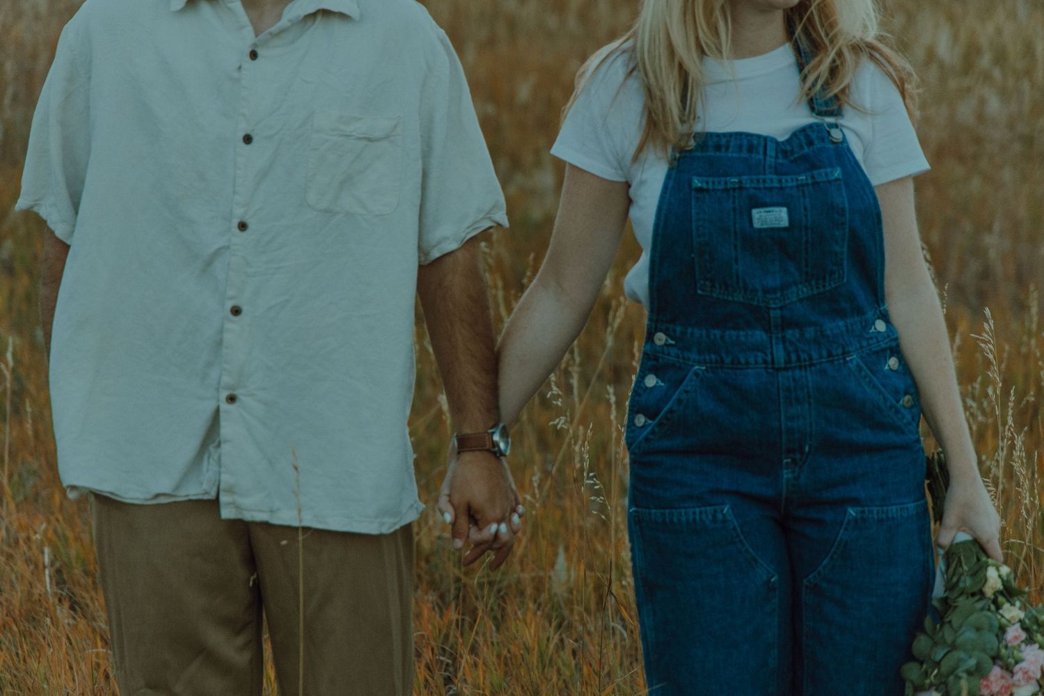 Couple standing facing camera next to each other holding hands in the middle