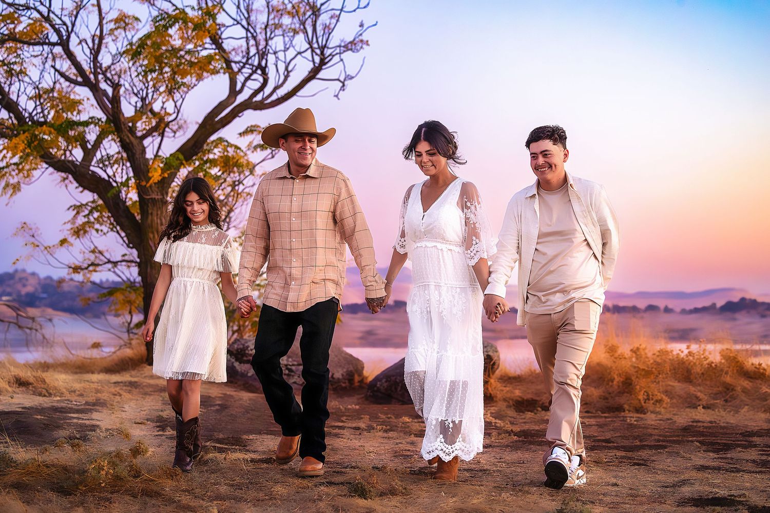 Family walking together on a desert trail at sunset with a lone tree in the background.