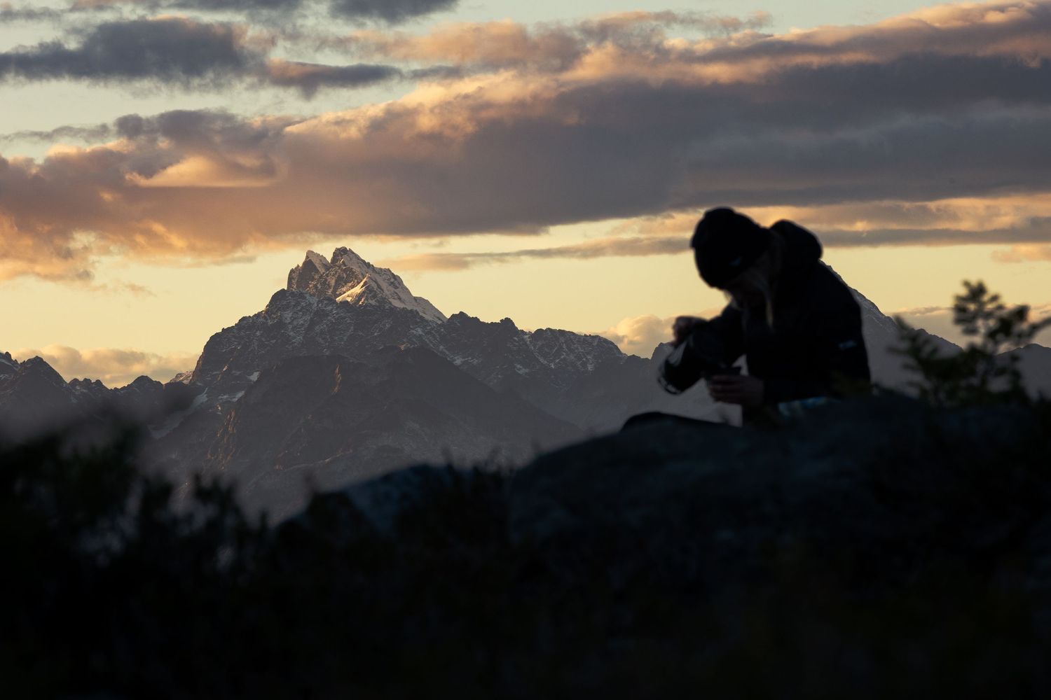 Silhouette of a photographer against majestic mountain peaks during sunset.