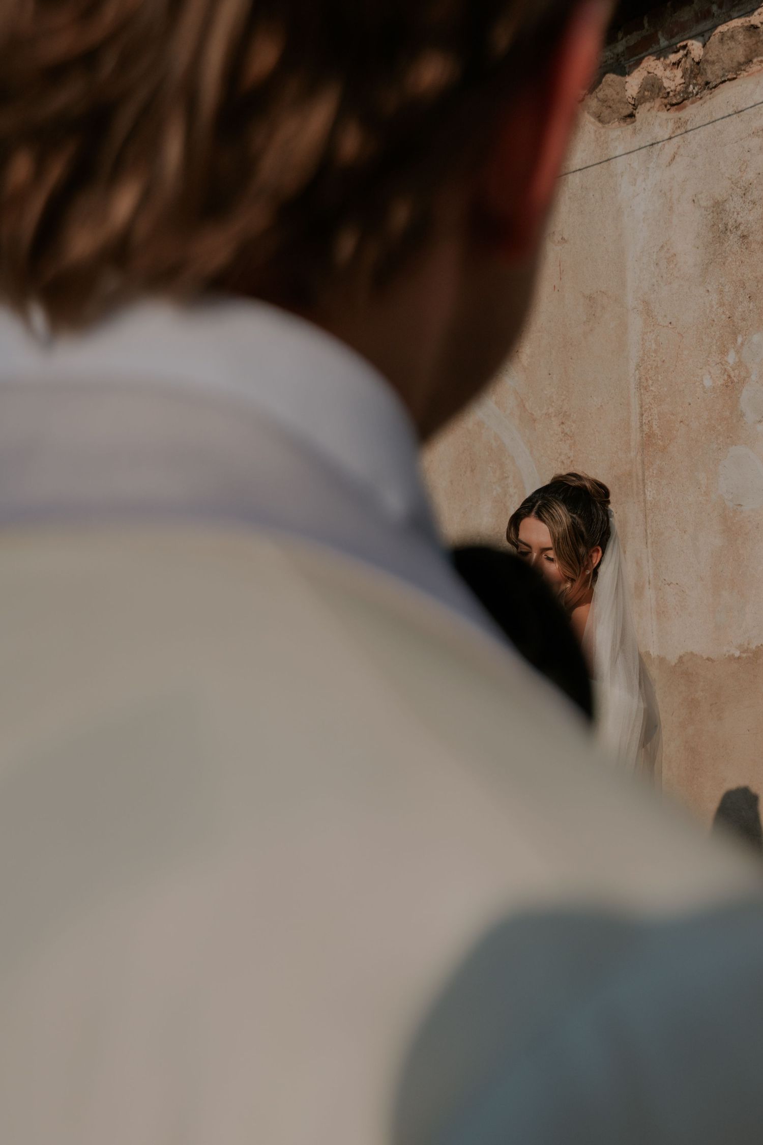 Black and white wedding photo of newlyweds embracing against a weathered stone wall backdrop.