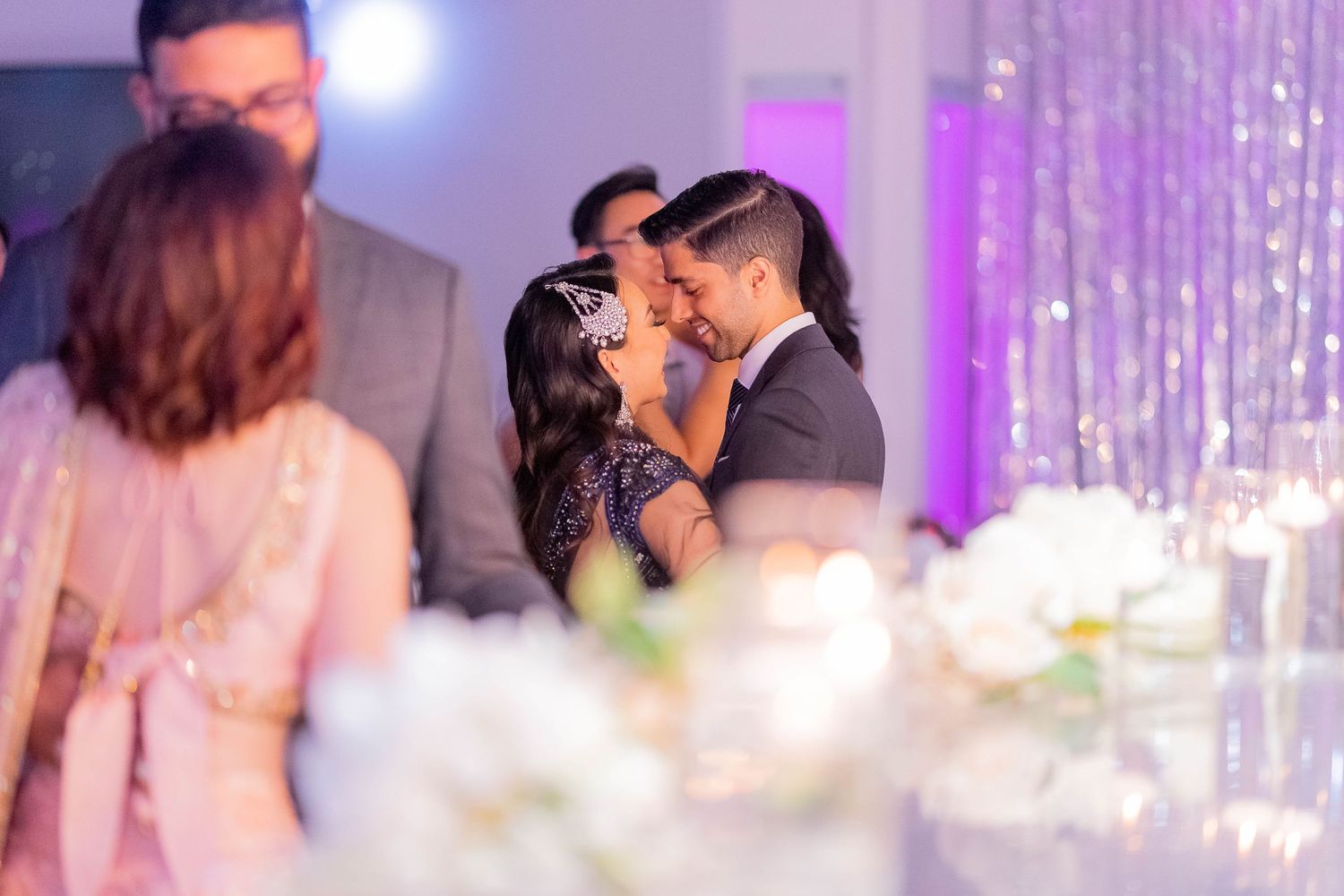 Romantic dance moment at wedding reception with purple lighting and sparkling backdrop.