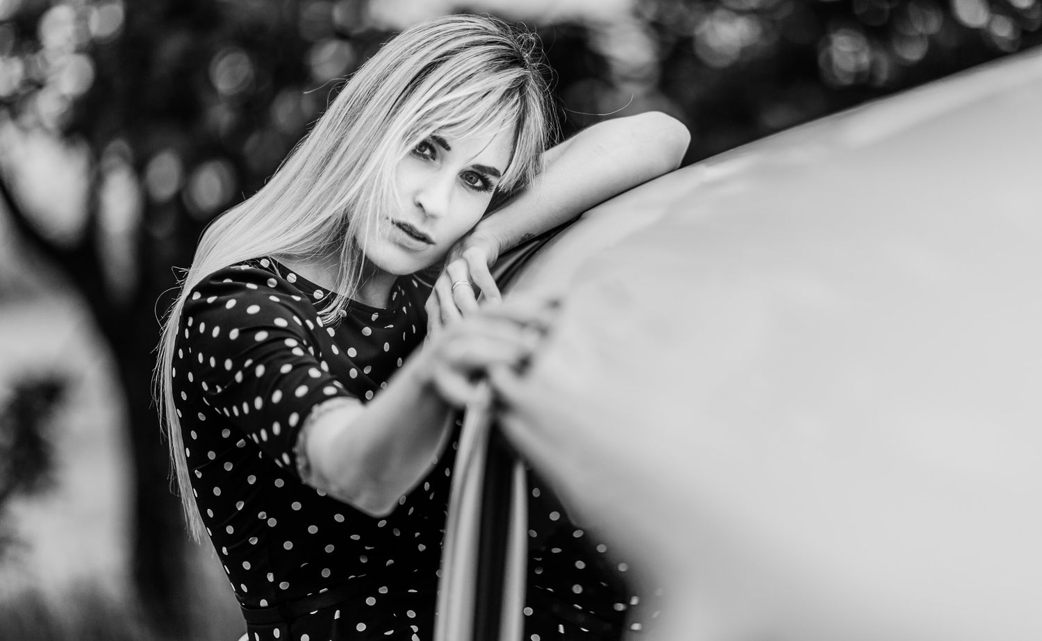 Black and white portrait of blonde woman leaning on vintage car.