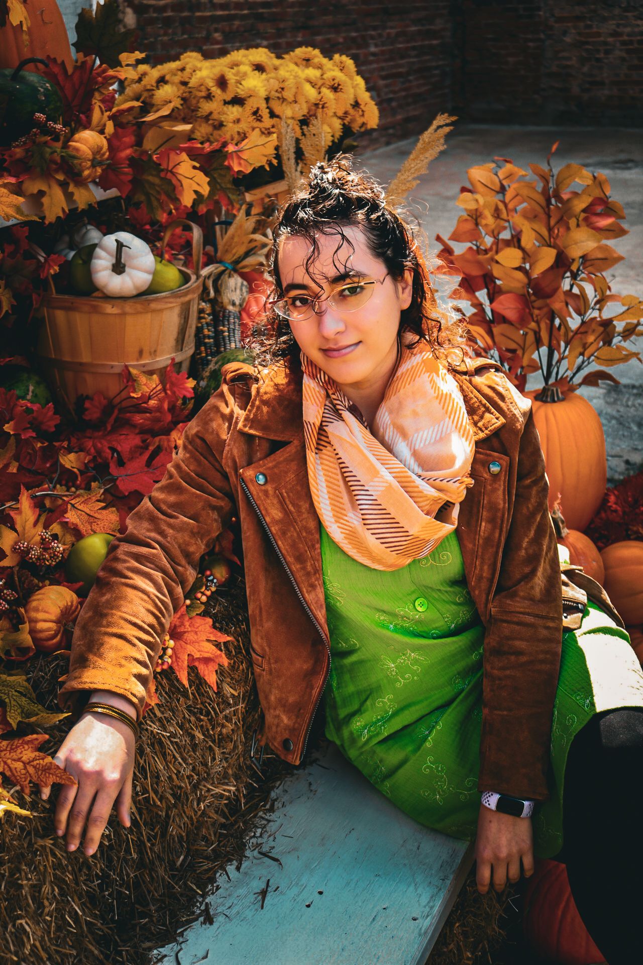 Smiling woman in red sweater holds a large pine cone outdoors surrounded by vibrant autumn foliage.