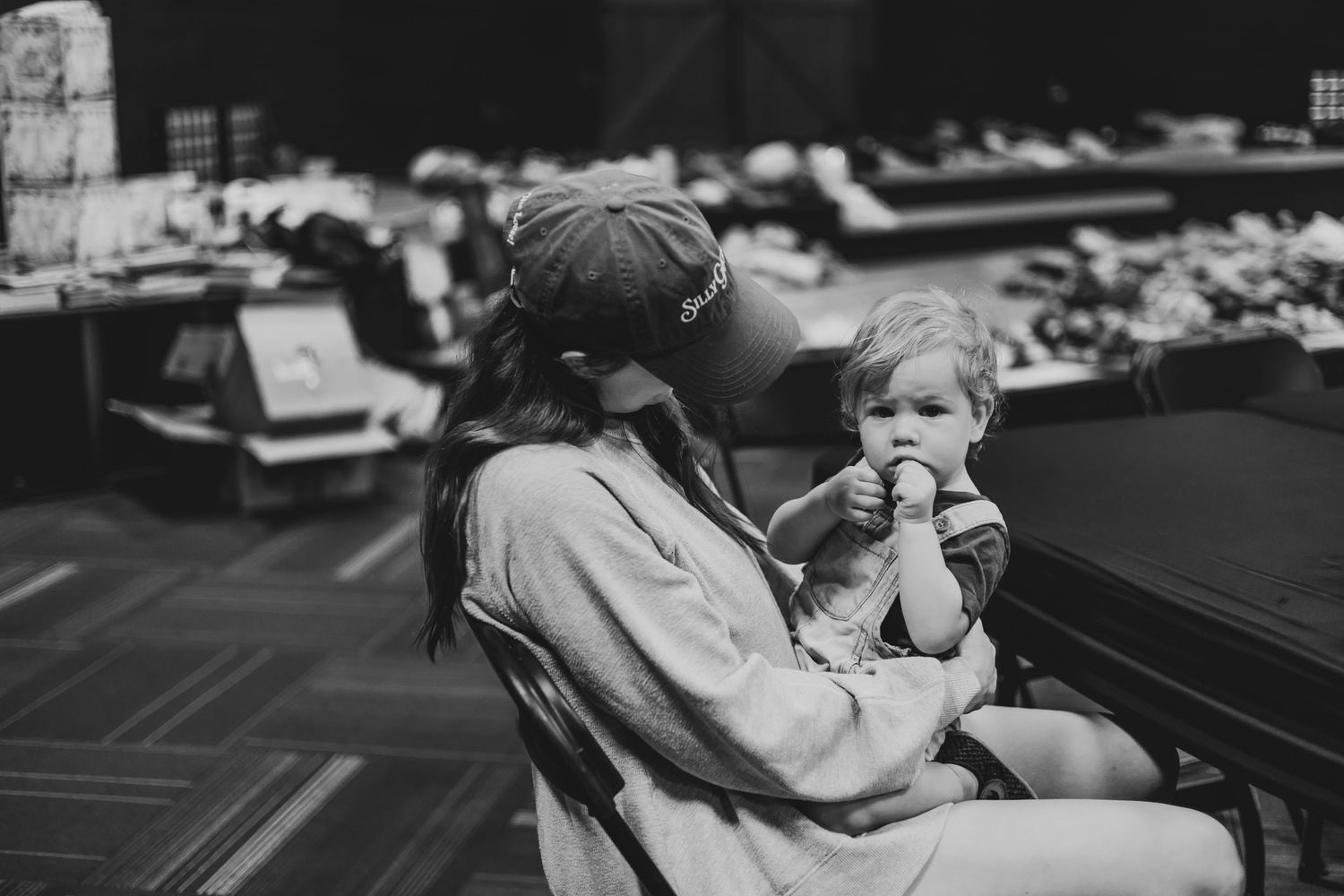 Black and white photo of a mother holding a young toddler while seated at a table indoors.