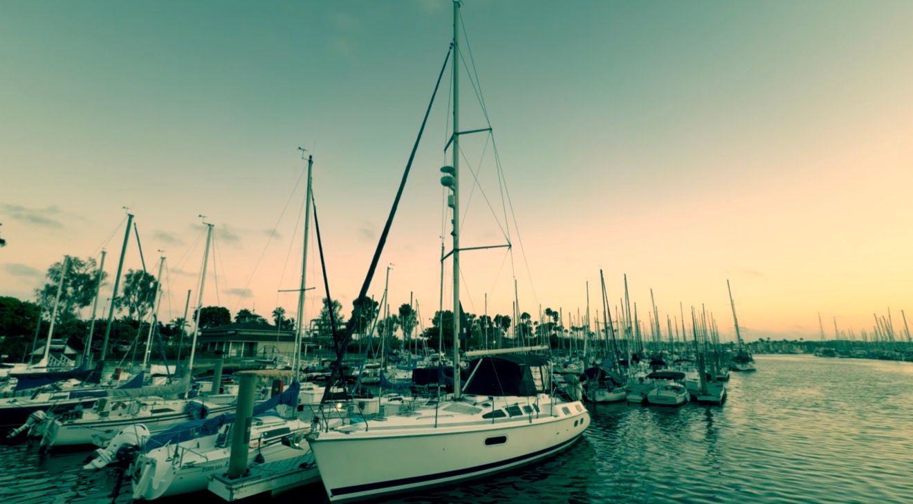 Sailboats docked at a marina during a golden sunset, with calm waters reflecting the warm sky.