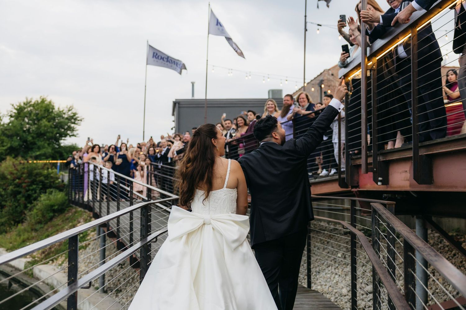 Wedding guests wave and cheer from a rustic wooden staircase as the newlyweds celebrate their special moment.